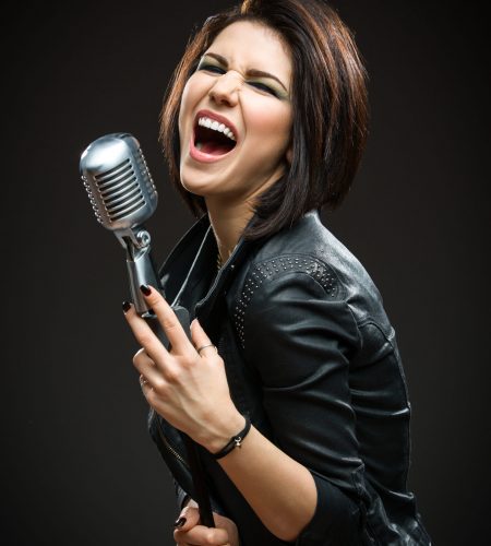 Half-length portrait of female rock musician wearing black jacket and keeping mike on grey background. Concept of music and rave